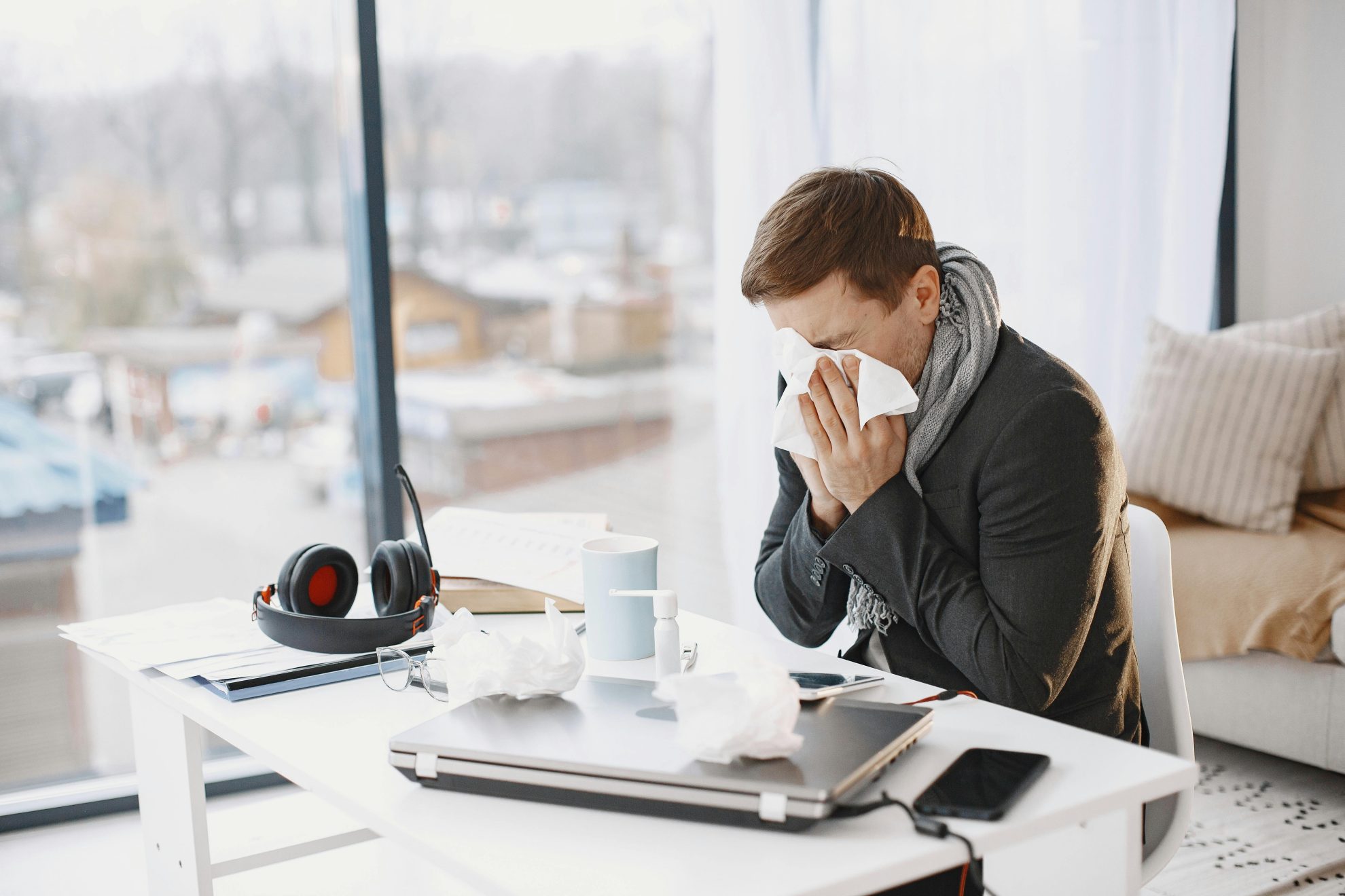 Man sneezing at home desk, indicating remote work during illness.